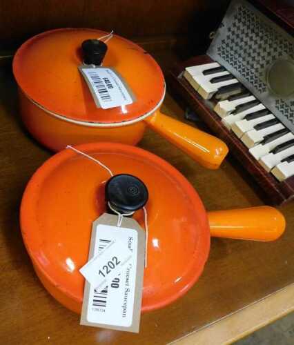 V - Two graduated Le Creuset pans, in orange, each with lids, 14cm high, etc. NB. VAT is payable on...