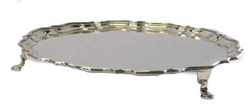 A George V silver salver, of circular form with a piecrust border, raised on three hoof feet,...