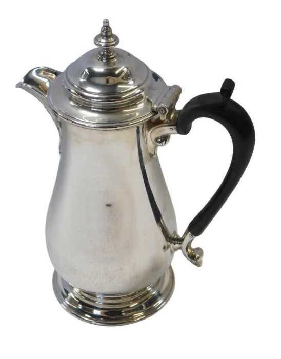 A George V silver hot water jug, of baluster form, with an ebonised handle, raised on a circular...