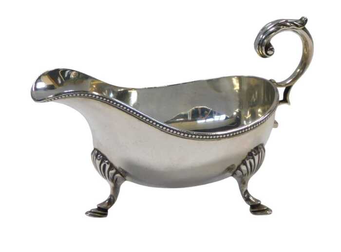 A late Victorian silver sauce boat, with an open acanthus handle and beadwork border, raised on...