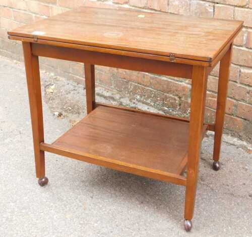A mahogany two tier folding card table, raised on castors.