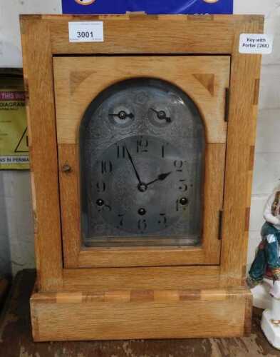 An early 20thC oak cased mantel clock, the arched silvered dial bearing Arabic numerals, with...