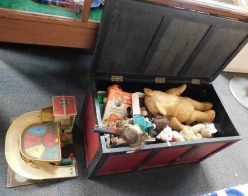A large toy chest, decorated in red and black, containing soft toys, and a plastic Fisher Price...