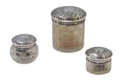 Three late Victorian cut glass and silver topped dressing table jars, each lid embossed with a...