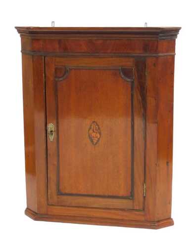 A George III mahogany hanging corner cupboard, with an outswept pediment over a panelled door...