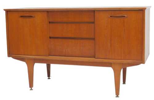 A mid-century teak sideboard, with three graduated frieze drawers, flanked by two sliding doors,...
