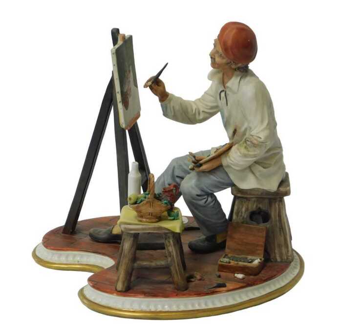 A Capodimonte porcelain figure, modelled as an artist seated at an easel, painting a still life,...