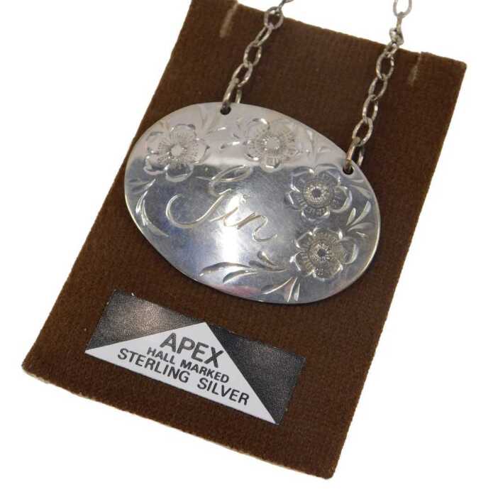A 20thC sterling silver gin label, of oval form, etched with flowers, with chain on apex...