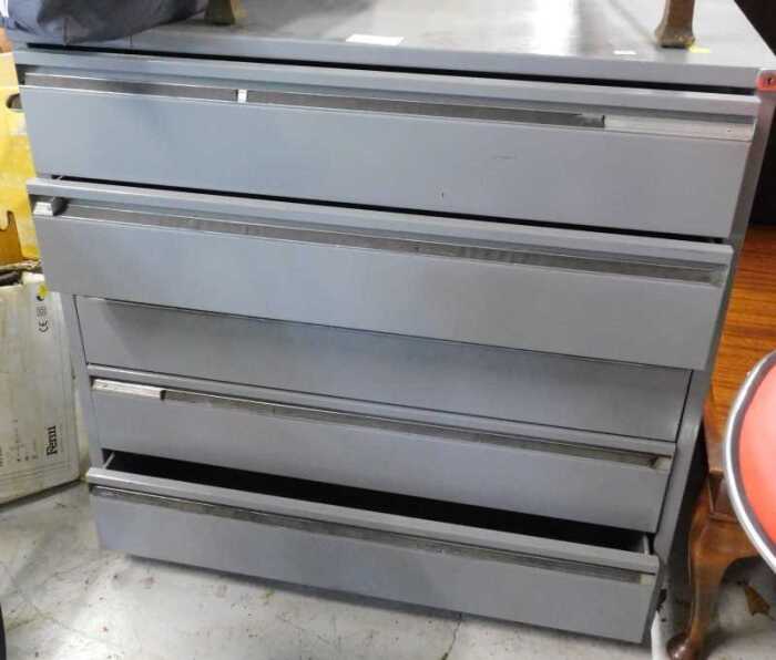 A grey metal five drawer plan chest, two red bar stools, and an oak carver chair.