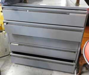 A grey metal five drawer plan chest, two red bar stools, and an oak carver chair.