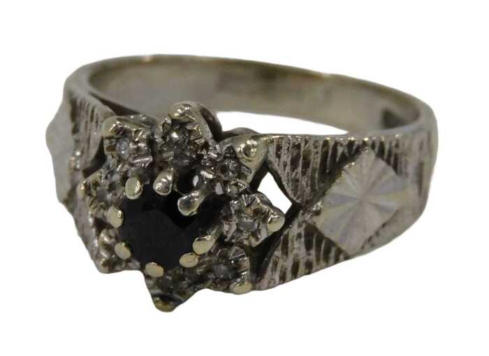 A 9ct white gold cluster ring, the central sapphire surrounded by eight tiny diamonds, on...