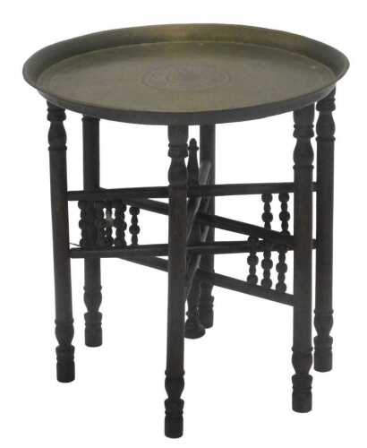 An early 20thC Eastern brass topped table, heavily decorated with scrolls and flowers, on an...