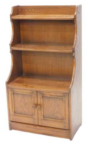 A late 20thC Ercol waterfall bookcase, with three shelves above double cupboards, 116cm high,...