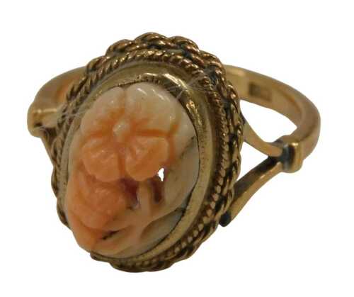 A coral dress ring, the oval carved coral formed as a flower, in a rub over and rope twist...