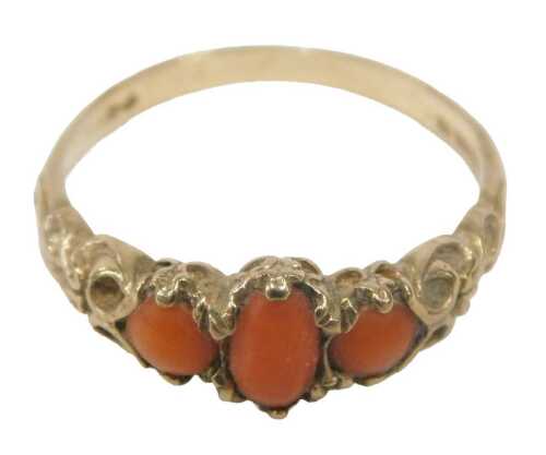 A 9ct gold coral dress ring, set with three coral stones, each claw set, in a heavily scrolled...