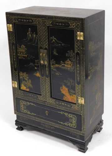 A Chinese lacquered cabinet, gilt decorated with river landscapes, having two doors opening to...