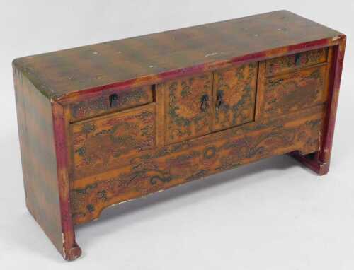 A Chinese red lacquered table cabinet, with two doors flanked by two short draws, decorated with...