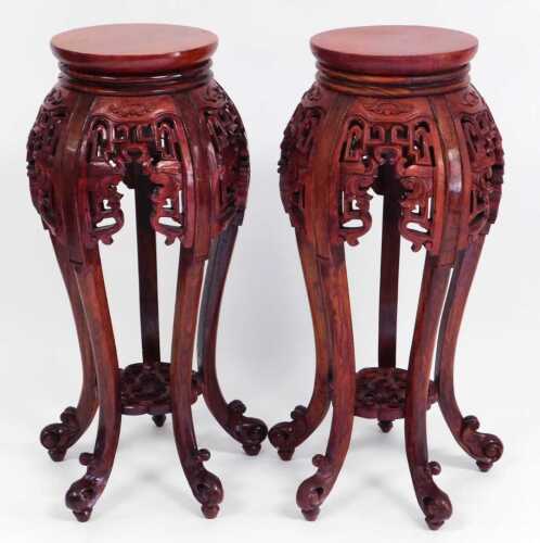 A pair of Chinese hardwood urn stands, stained red, each with a plain circular top, above...