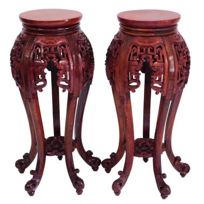 A pair of Chinese hardwood urn stands, stained red, each with a plain circular top, above...