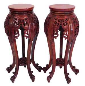 A pair of Chinese hardwood urn stands, stained red, each with a plain circular top, above...