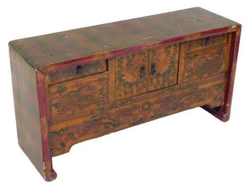 A Chinese red lacquered table cabinet, with two doors flanked by two short draws, decorated with...