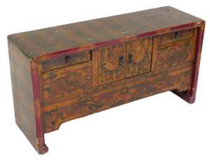 A Chinese red lacquered table cabinet, with two doors flanked by two short draws, decorated with...