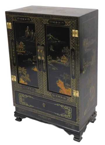 A Chinese lacquered cabinet, gilt decorated with river landscapes, having two doors opening to...