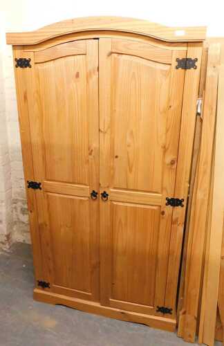 A pine double wardrobe, with an arched top, above two panelled doors enclosing two hanging rails,...