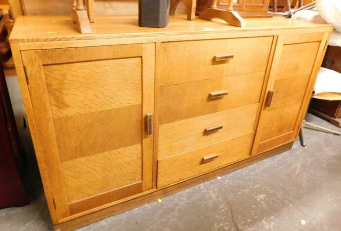 An oak sideboard, with four central drawers flanked by two panelled cupboards enclosing shelves,...