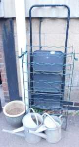Two galvanised watering cans, a terracotta plant pot, a three tier step ladder, and wire racking....