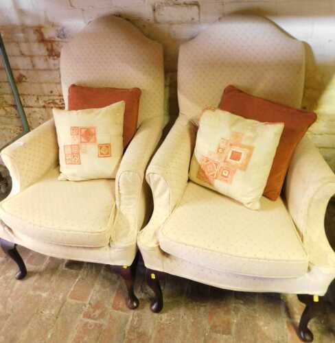 A pair of armchairs, upholstered in beige fabric, raised on oak cabriole legs with pad feet.