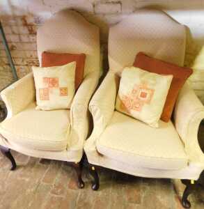 A pair of armchairs, upholstered in beige fabric, raised on oak cabriole legs with pad feet.