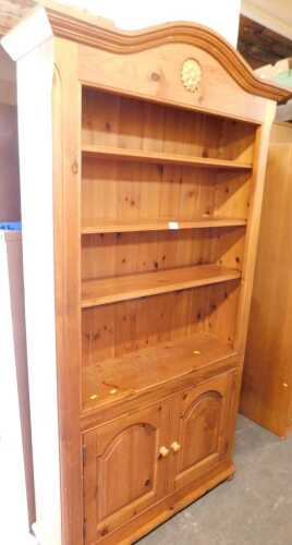 A pine open bookcase, the arched moulded top above a floral rosette, above three shelves, with...