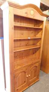 A pine open bookcase, the arched moulded top above a floral rosette, above three shelves, with...