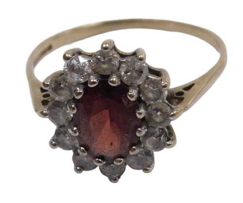 A 9ct gold garnet and cz ring, the oval cut garnet in a surround of brilliant cut czs, in a claw...