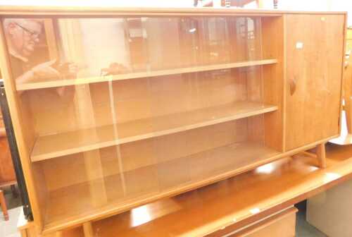 A teak bookcase, with two sliding glass doors flanked by a cupboard, raised on outswept legs,...