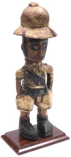 A 20thC African carving of a Colon figure, modelled standing in khaki dress, raised on a wooden...