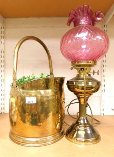 A Victorian brass oil lamp, converted to electricity, with a cranberry glass shade with ruffled...