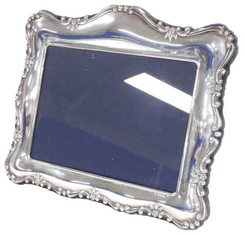 An Elizabeth II silver back strut photograph frame, the border embossed with flowers, leaves,...