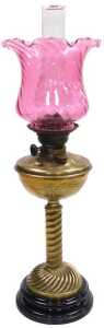 A Victorian brass oil lamp, the wrythen cranberry tinted shade, above a leaf decorated reservoir...