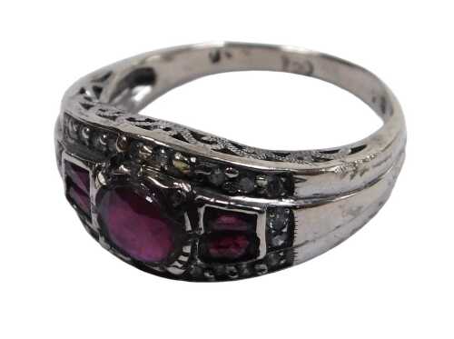 An Art Deco style ruby and diamond ring, the central brilliant cut ruby flanked by baguette cut...