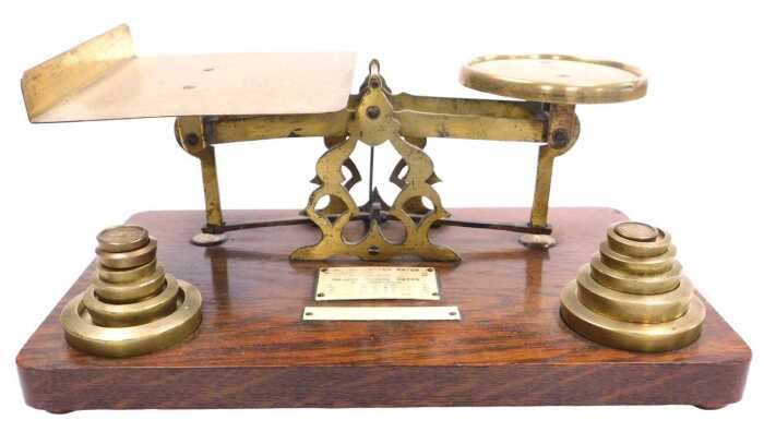 An early 20thC oak and brass set of postal scales, with ivorine plaque for Inland Letter Rates,...