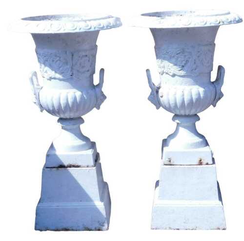 A pair of early 20thC white painted cast iron urns on stands, the urns of campana form with lion'...
