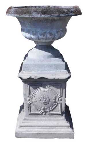 A stone garden urn on a stand, the urn of semi fluted form, with an everted rim, on a stepped...