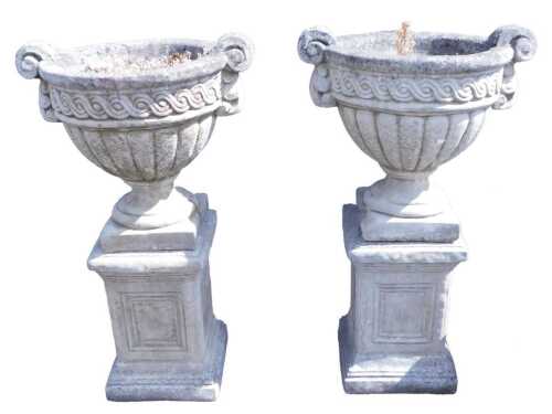 A pair of concrete urns on stands, the urns of semi fluted form, with a repeating scroll band...