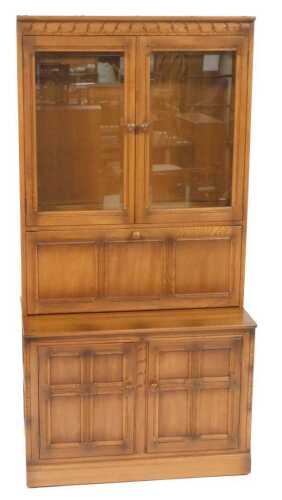An Ercol elm cupboard bookcase, the pediment over a pair of glazed doors enclosing two shelves,...