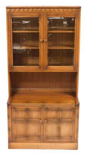An Ercol elm lounge unit, the pediment over a pair of glazed doors enclosing two shelves, over a...