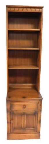 An Ercol elm display unit, with a pediment over three shelves, above a base with a frieze drawer...