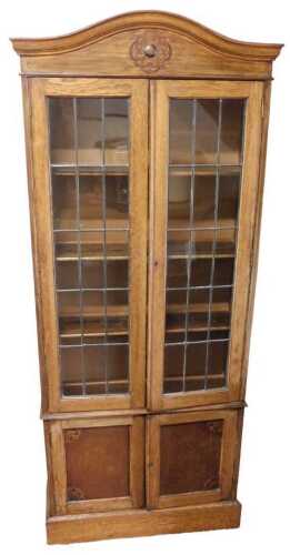 An early 20thC oak cupboard bookcase, with a domed pediment over a pair of astragal glazed doors...