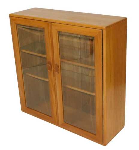An Ercol light elm display cabinet, with a pair of glazed doors enclosing two glass inset...
